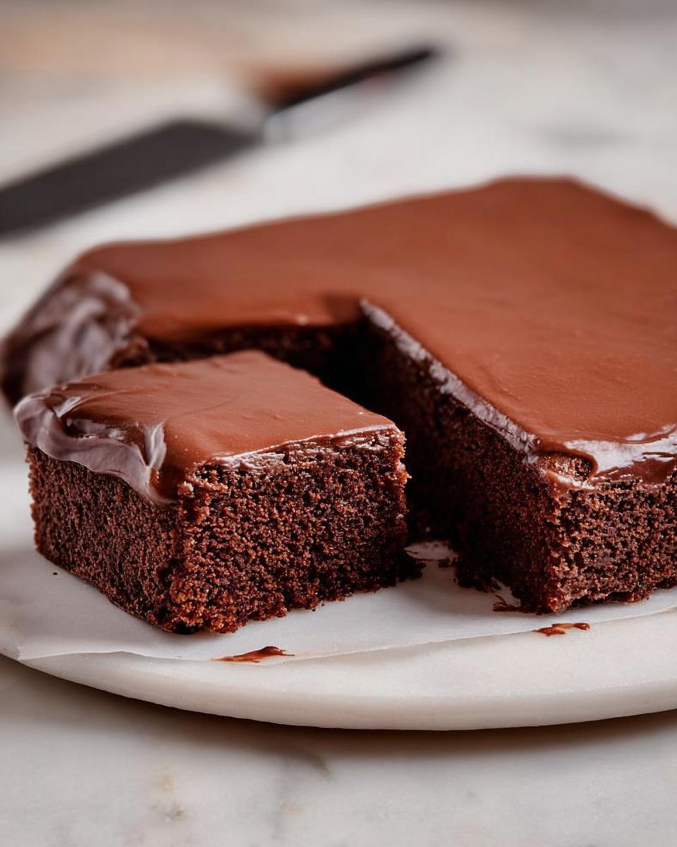 A slice of rich chocolate cake with glossy chocolate frosting, showcasing its moist crumb.