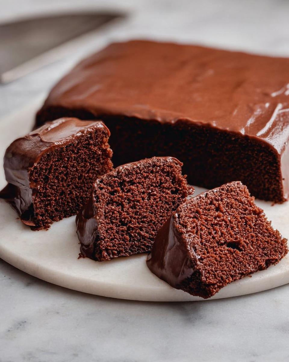 Three slices of rich chocolate cake with glossy frosting, part of a whole cake behind them.