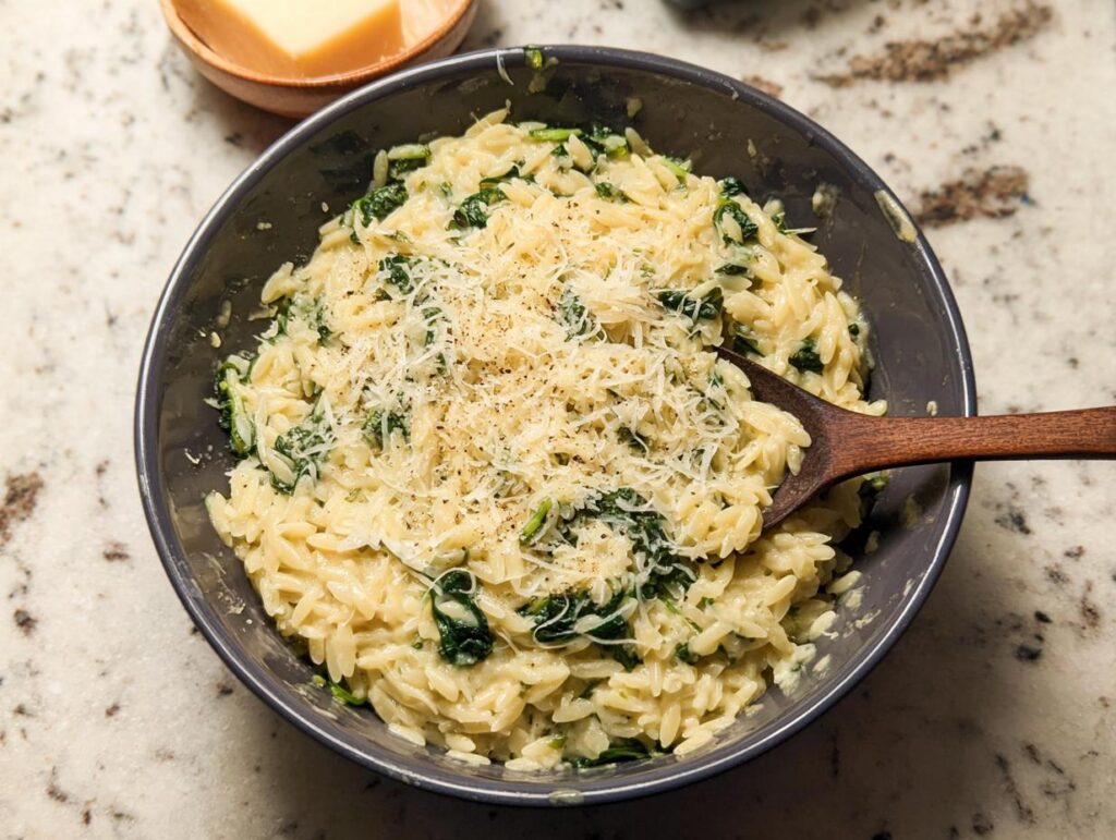 A close-up shot of creamy orzo with spinach, topped with grated Parmesan cheese, a perfect veggie sides recipe.