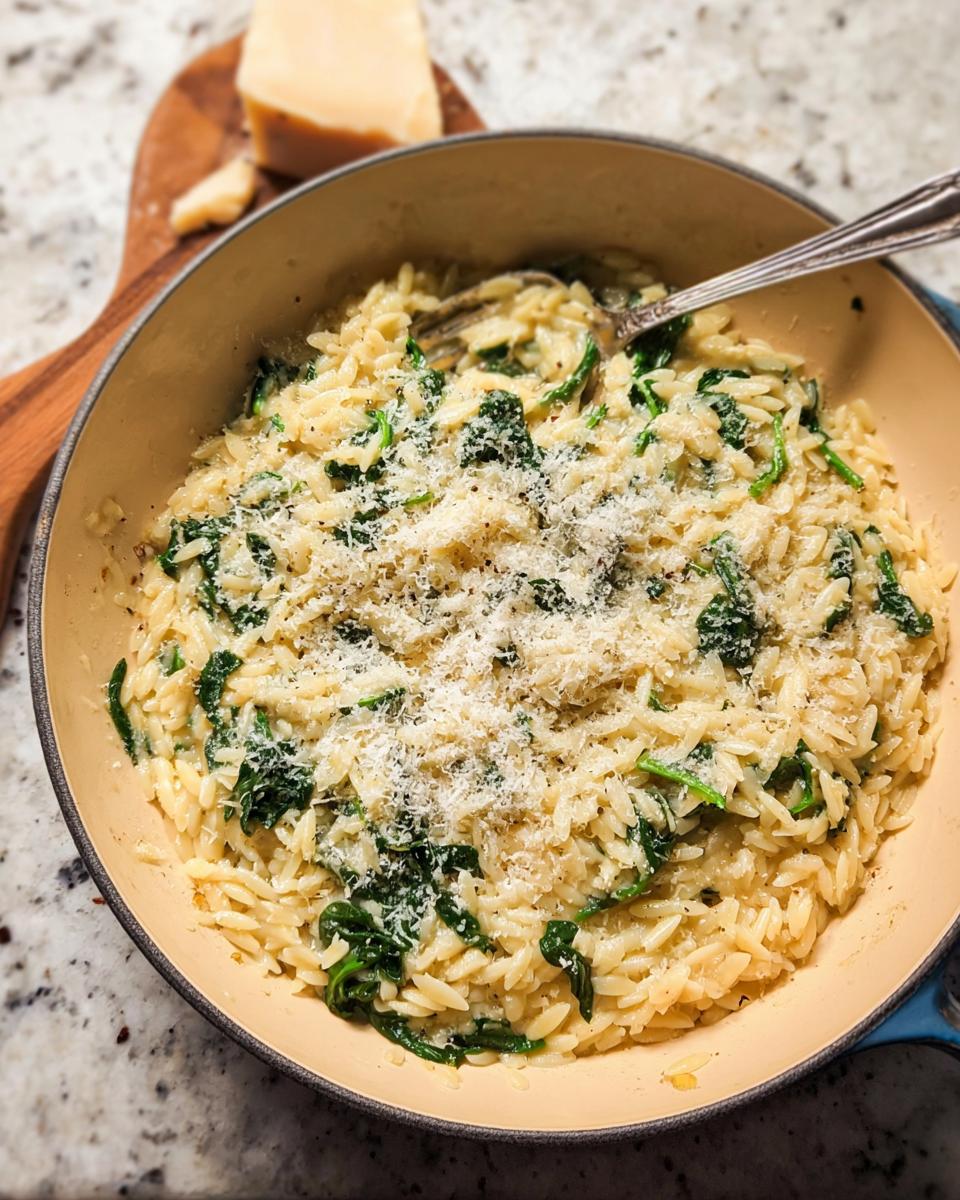 A close-up of creamy orzo pasta with wilted spinach, topped with grated Parmesan cheese, a perfect addition to your veggie sides recipes.