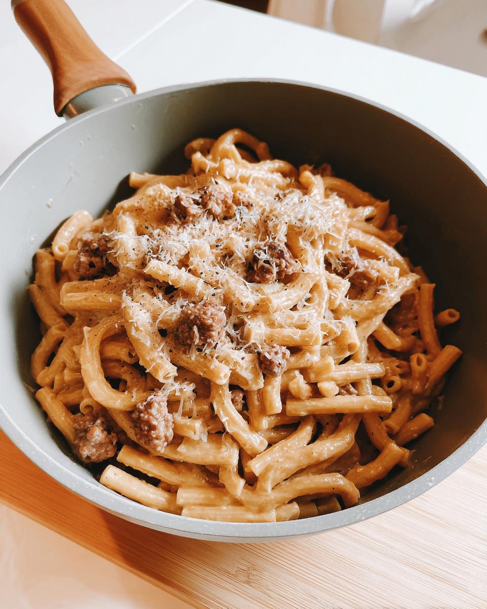 A close-up of creamy sausage pasta with grated cheese and black pepper in a pan, perfect for busy weeknights.