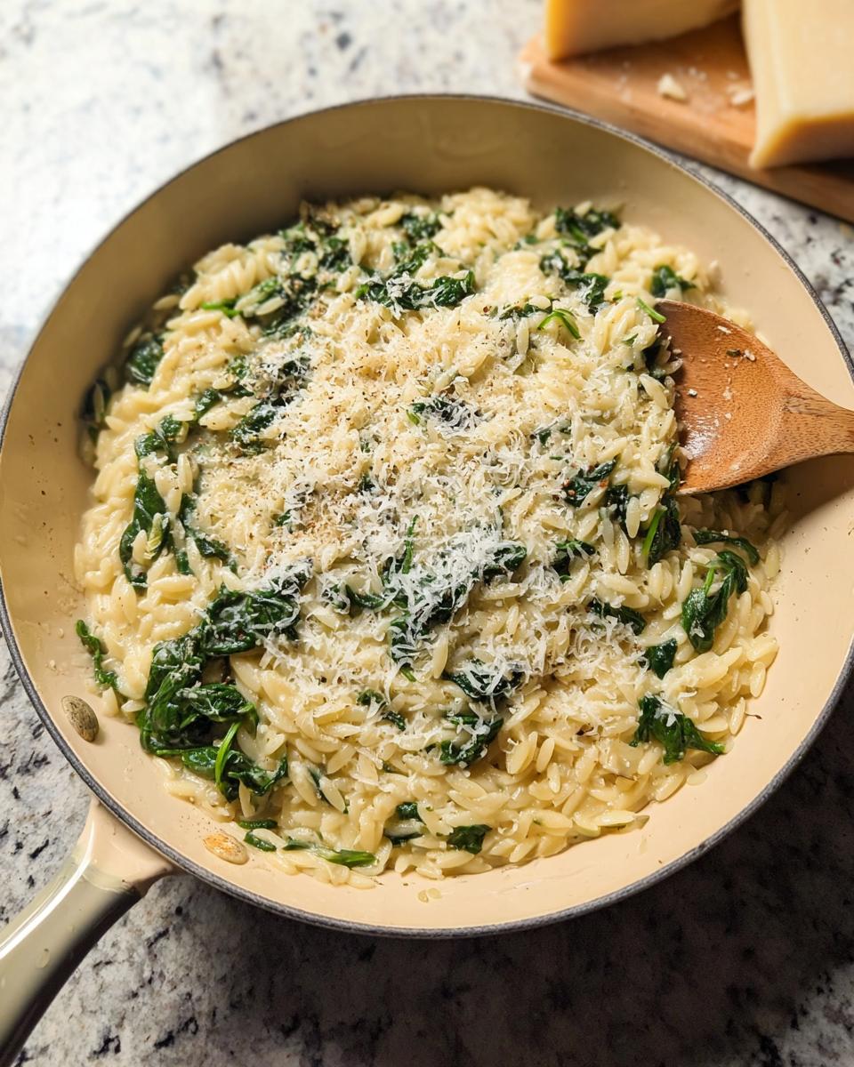 Close-up of creamy spinach orzo pasta in a pan, topped with grated Parmesan cheese.