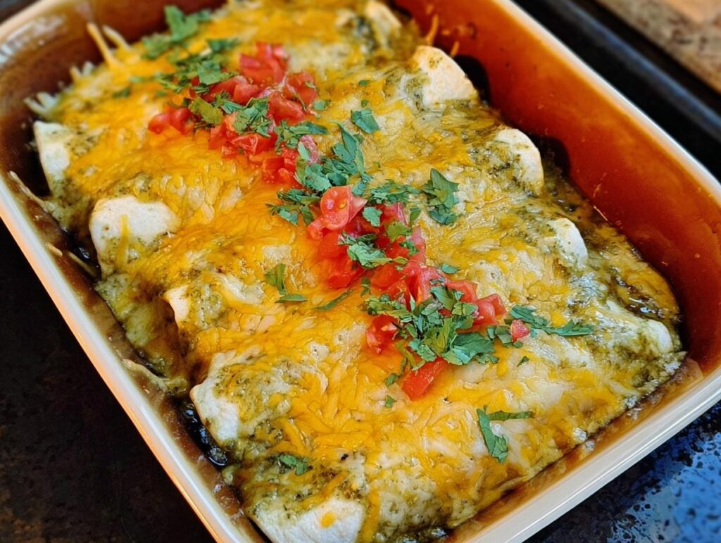 Close-up of baked green chile chicken enchiladas topped with melted cheese, diced tomatoes, and cilantro.