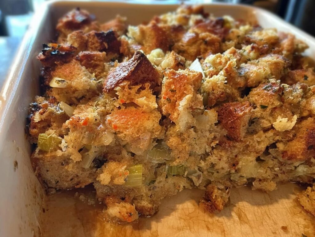 Close-up of a pan of delicious restaurant-style stuffing, featuring golden-brown bread cubes, celery, and herbs.