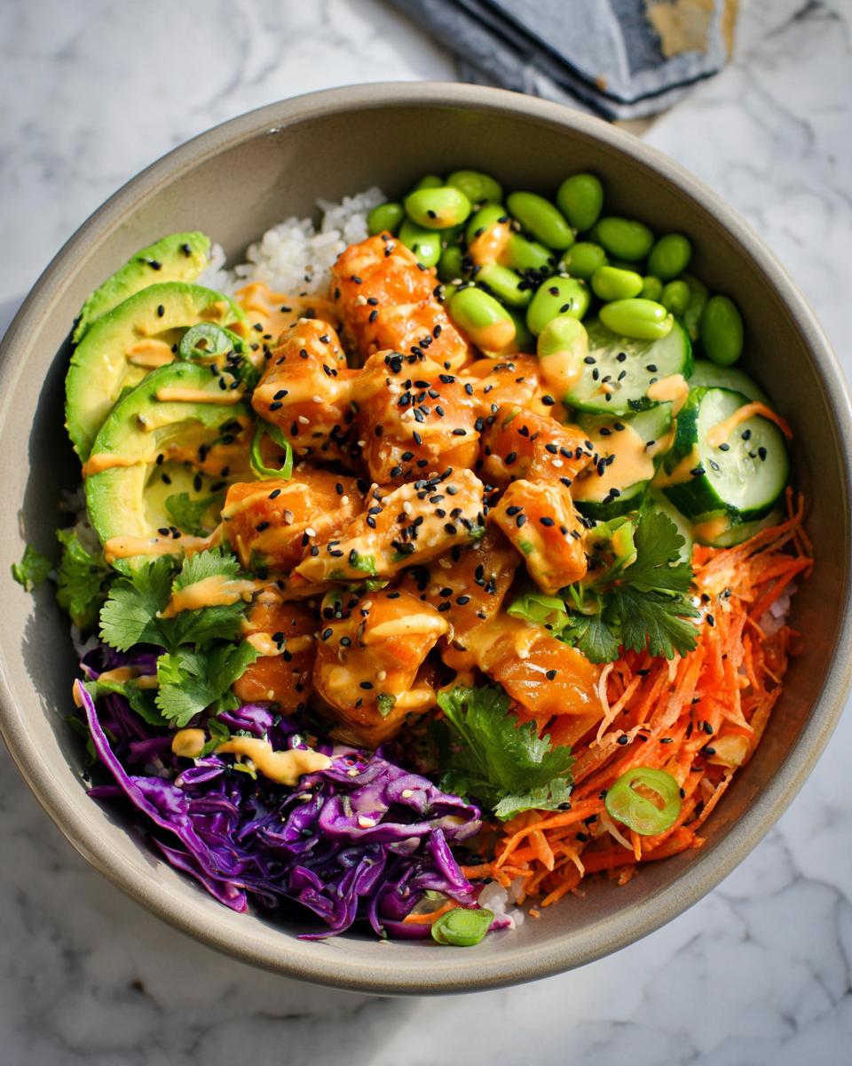 A vibrant bowl of Bang Bang Salmon Bites Bowls with rice, salmon, avocado, edamame, cucumber, and shredded carrots.