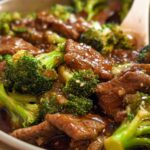 Close-up of a bowl of Chinese Beef and Broccoli, featuring tender beef slices and vibrant broccoli florets in a glossy sauce, sprinkled with sesame seeds.