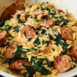 A close-up of creamy chicken sausage orzo with wilted spinach and grated Parmesan cheese.