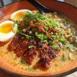 A close-up of a delicious bowl of Creamy Garlic Chicken Ramen, featuring sliced chicken, ramen noodles, a soft-boiled egg, and green onions.