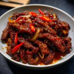 A bowl of Crispy Chilli Beef Rice, featuring tender beef strips coated in a glossy sauce with sliced red chillies and onions.