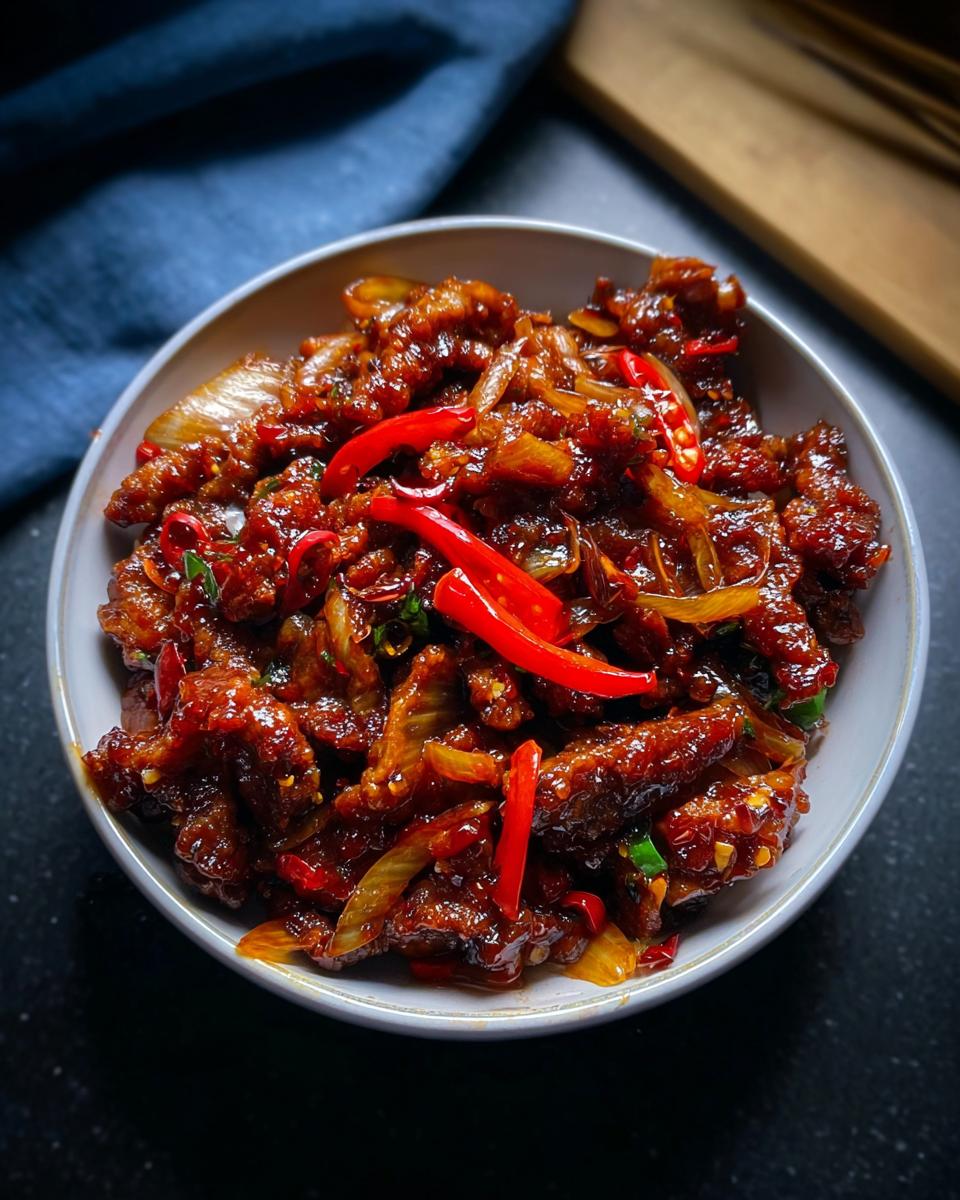 A close-up shot of a bowl filled with Crispy Chilli Beef Rice, garnished with fresh red chillies and onions.