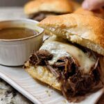 Close-up of a delicious Crockpot French Dip Sandwich overflowing with shredded beef and melted cheese, served with a side of au jus.