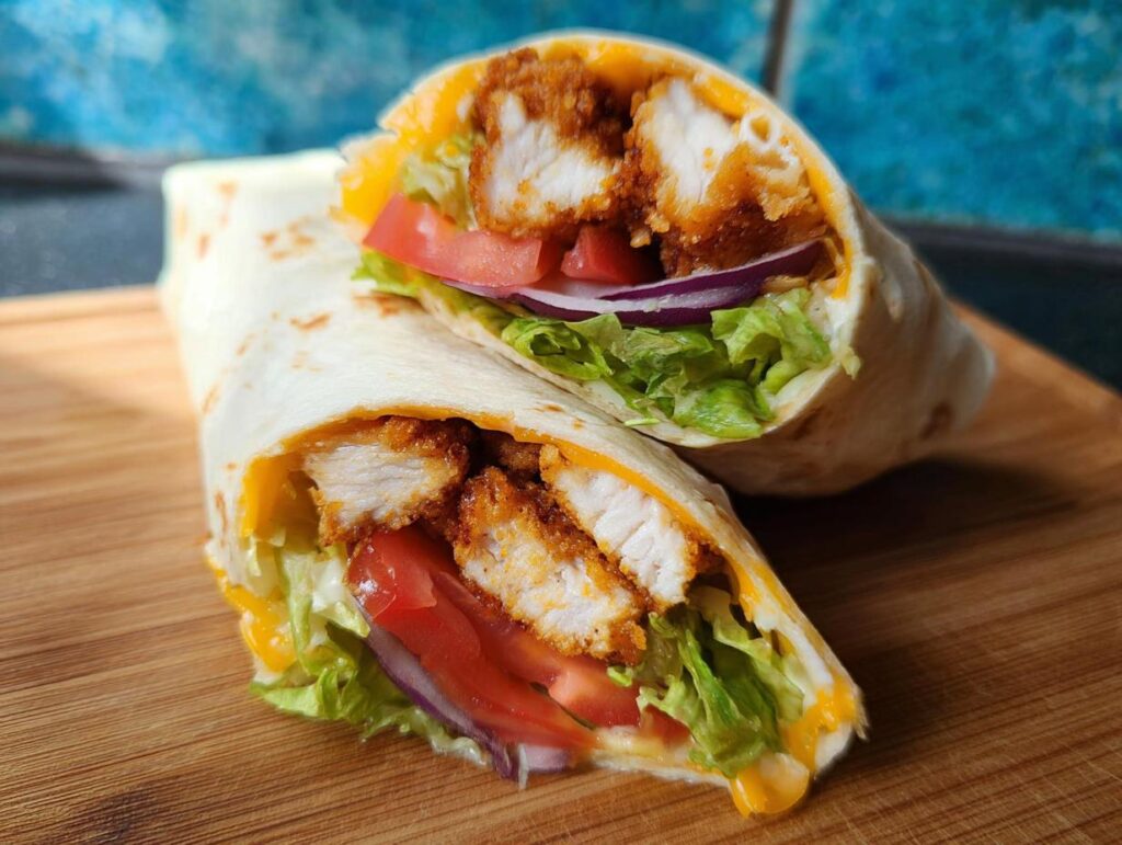 Two halves of a crunchy crispy air fryer chicken and mozzarella wrap filled with lettuce, tomato, and red onion.