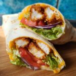 Two halves of a crunchy crispy air fryer chicken and mozzarella wrap filled with lettuce, tomato, and red onion.