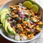 A vibrant Easy Street Corn Chicken Bowl filled with rice, seasoned chicken, corn, avocado slices, red onion, and lime wedges.