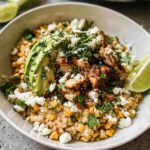 A vibrant Easy Street Corn Chicken Bowl topped with sliced avocado, crumbled cheese, and fresh cilantro, served with lime wedges.