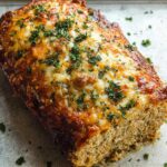 A close-up of a golden-brown Garlic Parmesan Chicken Meatloaf topped with melted cheese and fresh parsley.