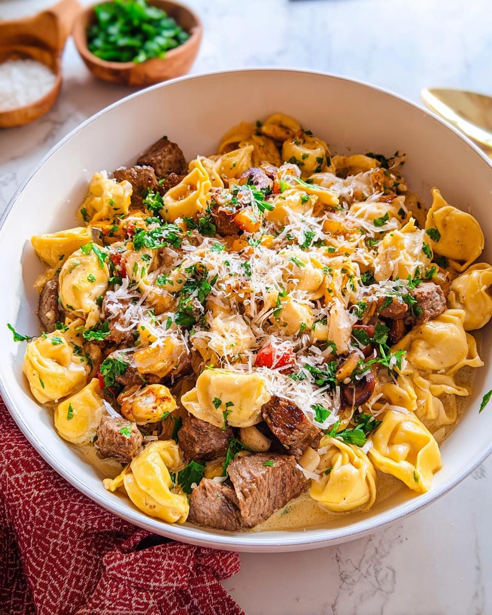 A close-up of a bowl filled with Garlic Steak Tortellini, featuring tender steak pieces and cheese-filled pasta in a rich sauce, garnished with parsley and Parmesan.
