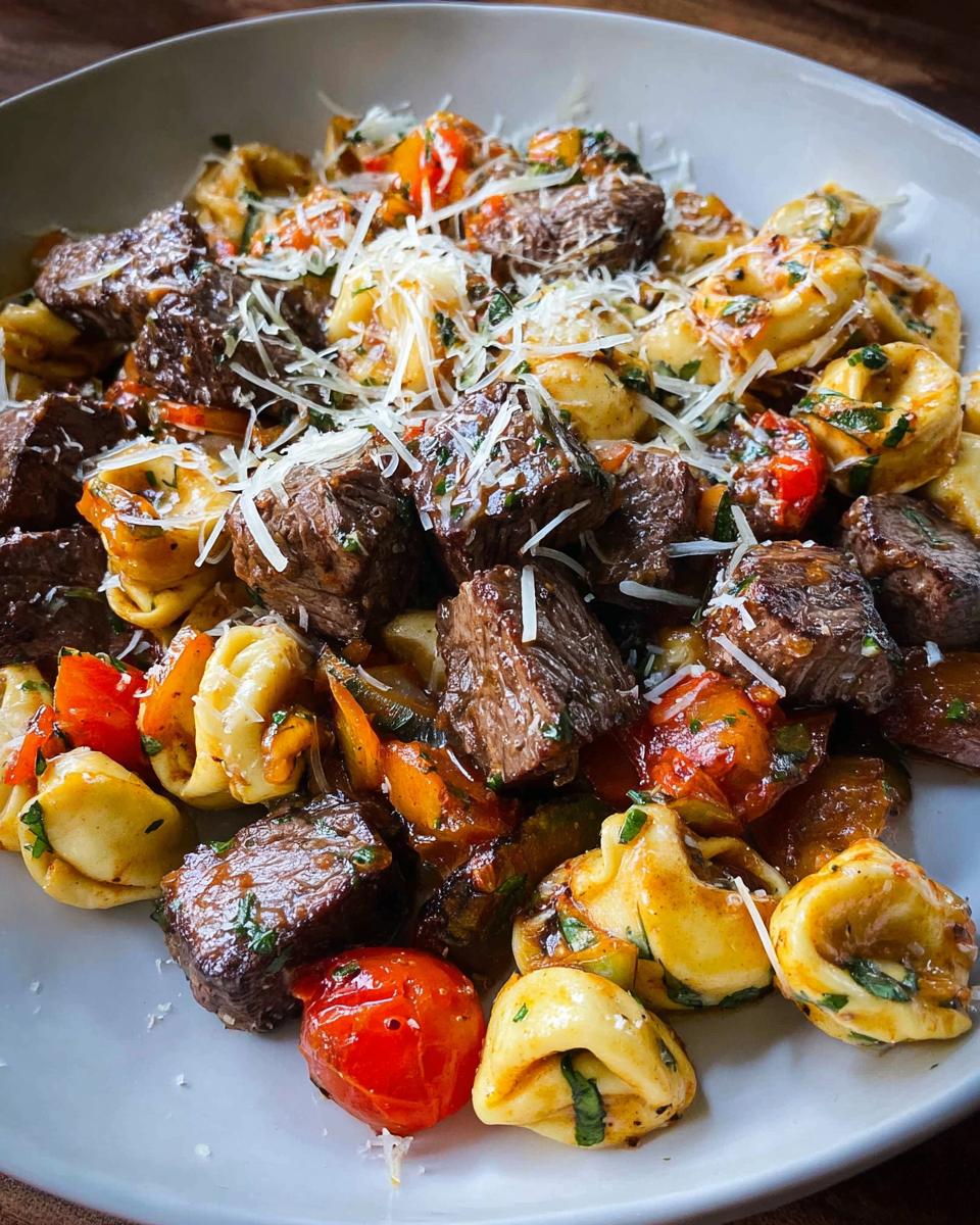 A close-up of a white bowl filled with Garlic Steak Tortellini, featuring tender steak bites, cheese tortellini, cherry tomatoes, and zucchini.