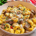 A close-up of a white pan filled with Garlic Steak Tortellini, garnished with parsley and grated cheese.