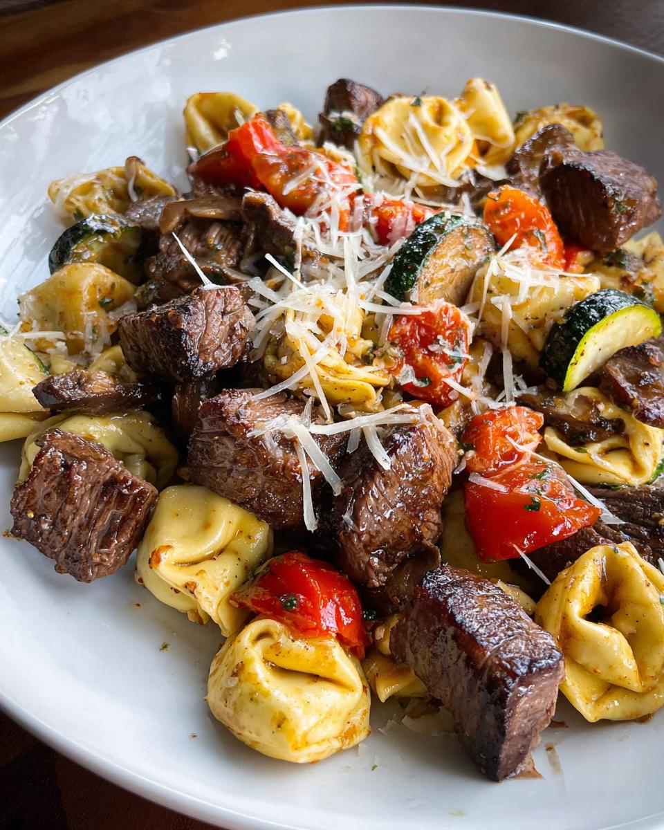 A close-up of Garlic Steak Tortellini mixed with grilled zucchini, cherry tomatoes, and topped with shredded parmesan cheese.