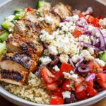 A delicious bowl of Greek Chicken Bowls, featuring grilled chicken, quinoa, tomatoes, cucumbers, red onion, olives, and feta cheese.