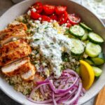 A vibrant bowl of Greek Chicken Bowls featuring sliced chicken, cucumber, tomatoes, red onion, and tzatziki sauce.