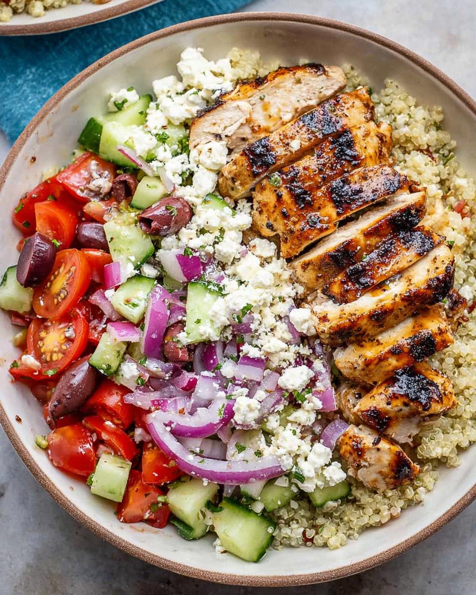 A delicious bowl of Greek Chicken Bowls with grilled chicken, quinoa, tomatoes, cucumbers, olives, red onion, and feta cheese.