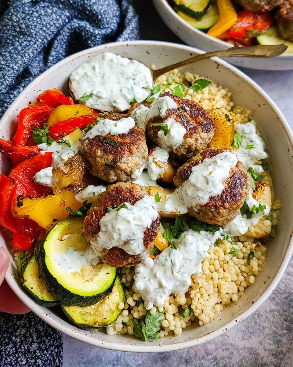 A delicious Greek Meatball Bowl filled with couscous, roasted vegetables, and topped with meatballs and tzatziki sauce.