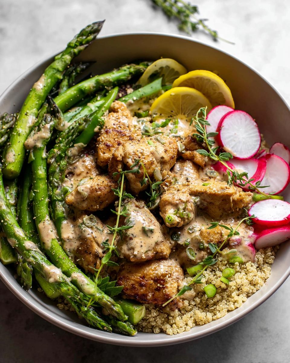 A healthy lemon garlic chicken meal prep bowl with quinoa, asparagus, radishes, and lemon slices.