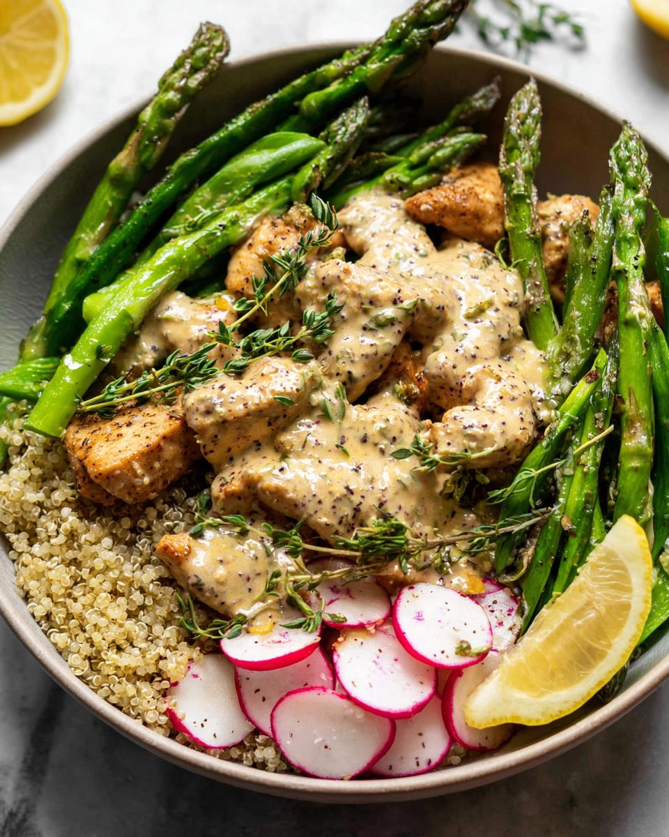 A healthy lemon garlic chicken meal prep bowl with quinoa, asparagus, radishes, and a creamy sauce.