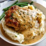 A succulent piece of Irresistible Garlic Herb Chicken served over a generous portion of creamy mashed potatoes, drizzled with sauce and garnished with parsley.