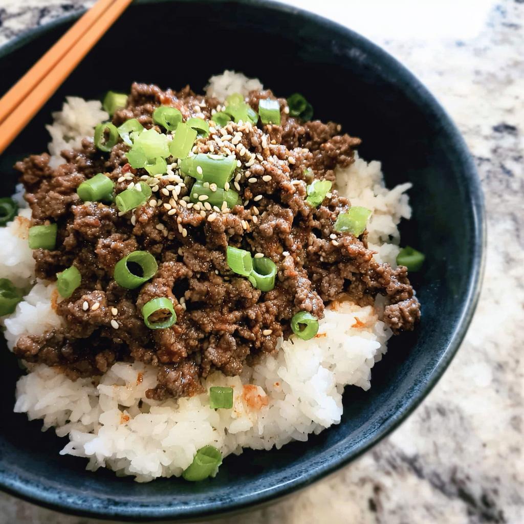 A close-up of a Korean Ground Beef Bowl, featuring seasoned ground beef over white rice, garnished with green onions and sesame seeds.