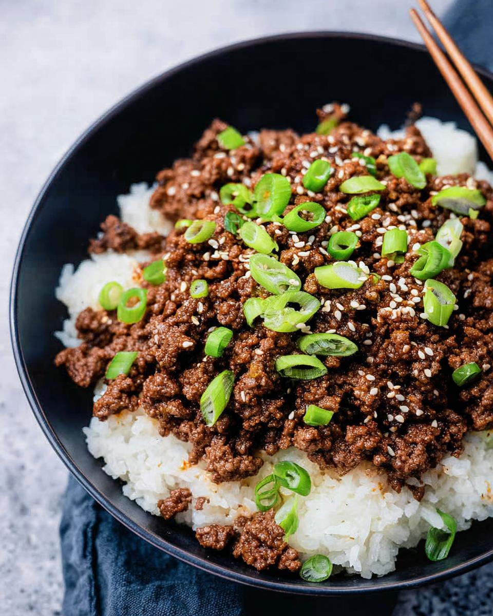 A close-up of a Korean Ground Beef Bowl, featuring savory ground beef over white rice, topped with sesame seeds and chopped green onions.
