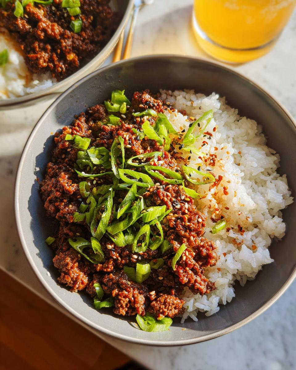 A close-up of a Korean Ground Beef Bowl, featuring seasoned ground beef over white rice, topped with chopped scallions and sesame seeds.