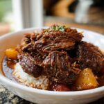 A bowl of Korean Style Pot Roast served over white rice, with tender shredded beef and vegetables in a rich sauce.
