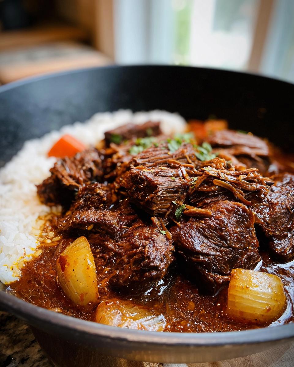 Close-up of tender Korean Style Pot Roast served over fluffy white rice with chunks of onion and a rich, dark sauce.