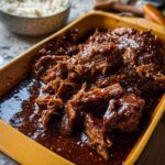 A close-up of tender Korean Style Pot Roast in a glossy, dark sauce, sprinkled with sesame seeds.