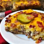 A slice of Low-Carb Bacon Cheeseburger Casserole topped with melted cheese, bacon, and a pickle slice.