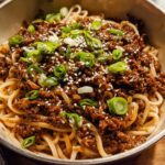 A close-up of a bowl of Mongolian Ground Beef Noodles, topped with green onions and sesame seeds.