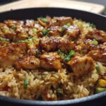 A close-up of a one-pan honey BBQ chicken rice dish, featuring glazed chicken pieces over seasoned rice with vegetables.