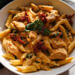 A close-up of creamy Parmesan Marry Me Chicken Pasta with penne, chicken pieces, sun-dried tomatoes, and basil.