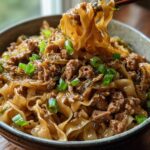 A close-up of a Potsticker Noodle Bowl with Pork and Cabbage, with noodles being lifted by chopsticks.