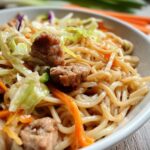 Close-up of a Potsticker Noodle Bowl with tender pork pieces, noodles, and a fresh cabbage slaw.