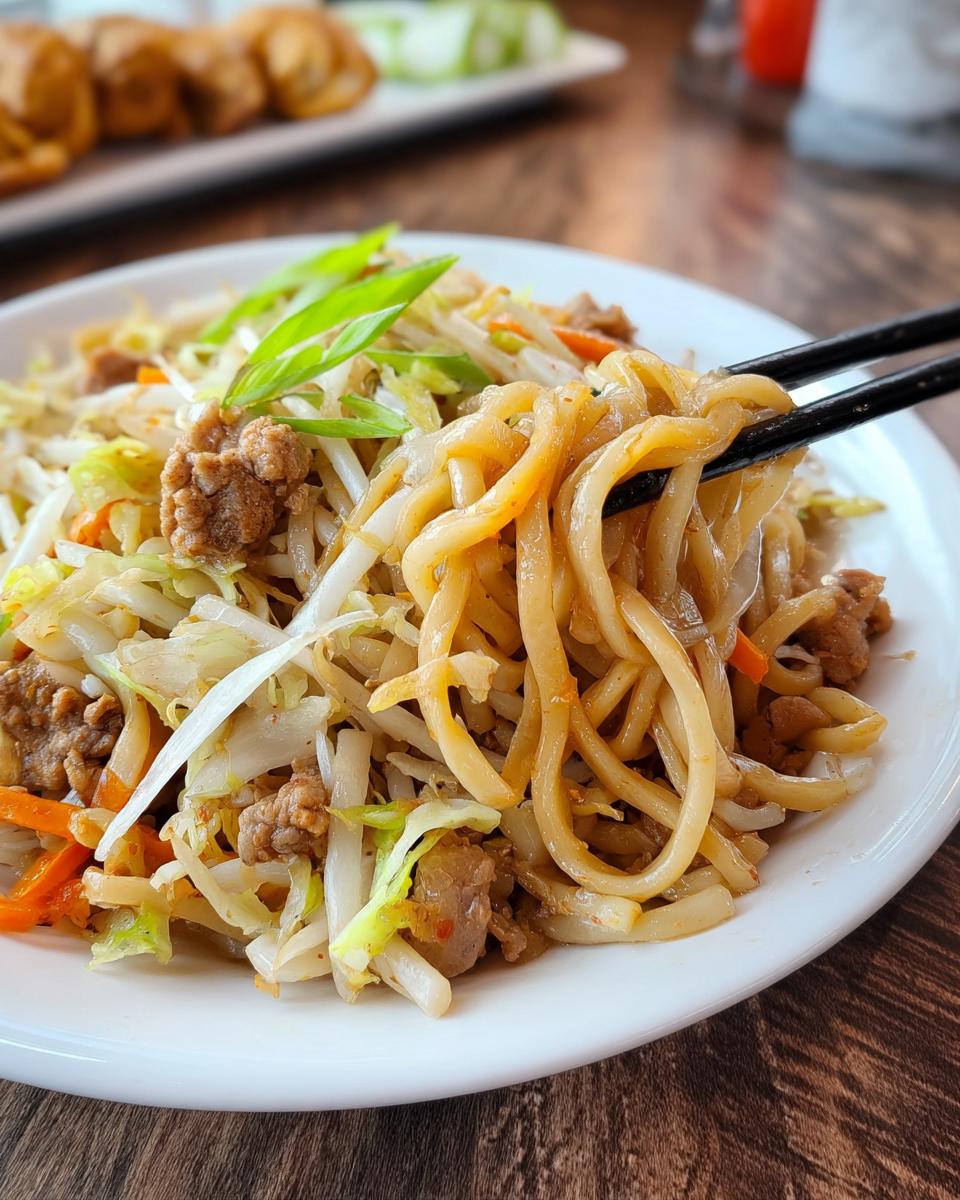 A close-up of a Potsticker Noodle Bowl with Pork & Cabbage Slaw, featuring thick noodles, tender pork, and fresh vegetables.