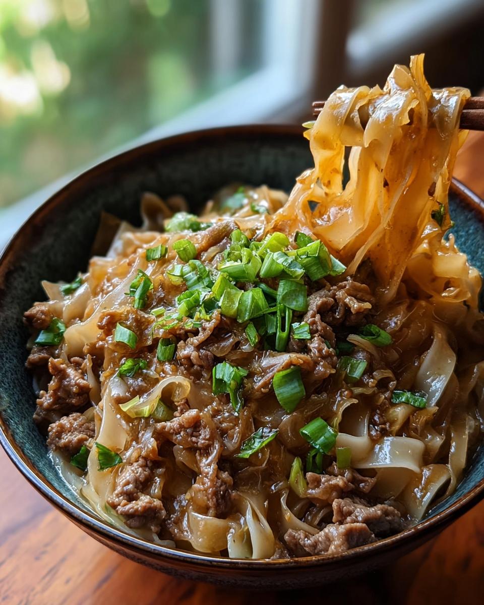 A close-up of a potsticker noodle bowl with tender pork, wide noodles, and fresh green scallions.