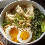 A close-up of a Savory Dumpling Ramen Bowl with soft-boiled eggs, dumplings, greens, and noodles.