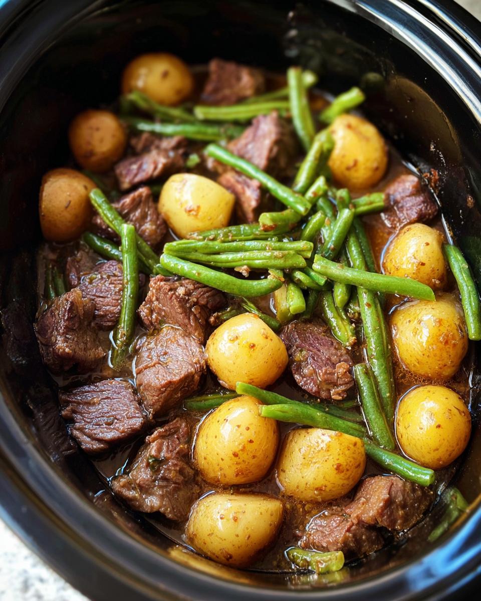 Close-up of Slow Cooker Garlic Butter Beef with Potatoes and green beans in a black crock pot.
