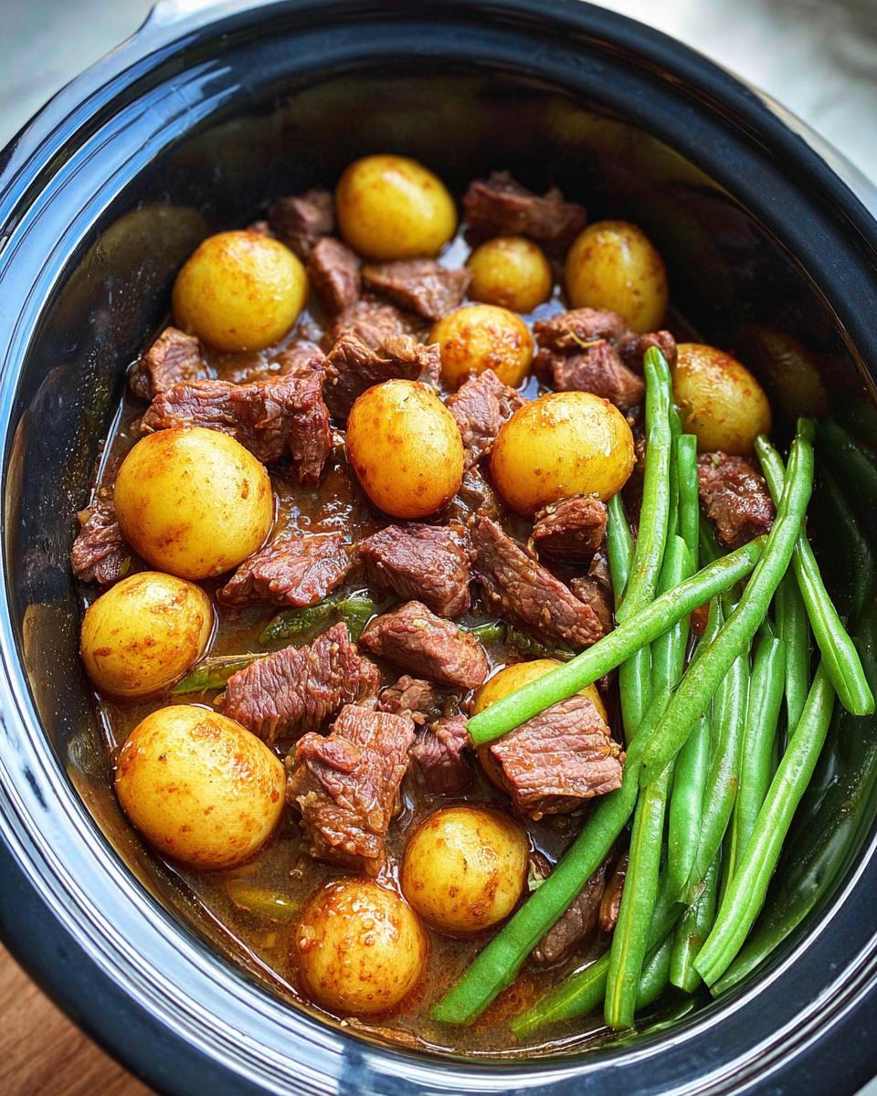 A close-up overhead view of a slow cooker filled with tender chunks of garlic butter beef, whole potatoes, and fresh green beans.