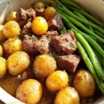 Close-up of Slow Cooker Garlic Butter Beef with Potatoes and Green Beans in a white ceramic pot.