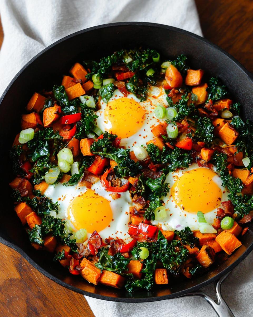 A close-up of a cast-iron skillet filled with a colorful BREAKFAST SWEET POTATO hash, topped with sunny-side-up eggs and green onions.